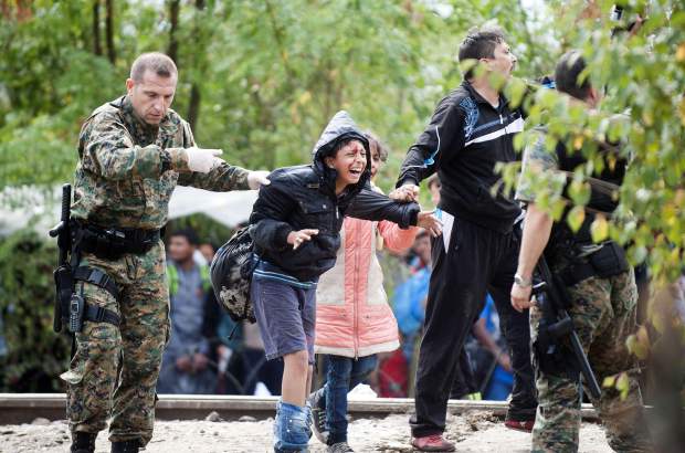 TOPSHOTS A member of the Macedonian police force and a migrant hold an injured boy during a clash between Macedonian police forces and migrant trying to cross an illegal crossing point on the border between Greece and Macedonia near the town of Gevgelija on August 22, 2015. Hundreds of mostly Syrian refugees forced their way over the Macedonian border today as police hurled stun grenades in a failed bid to stop them breaking through, an AFP reporter said. AFP  PHOTO / ROBERT ATANASOVSKIROBERT ATANASOVSKI/AFP/Getty Images